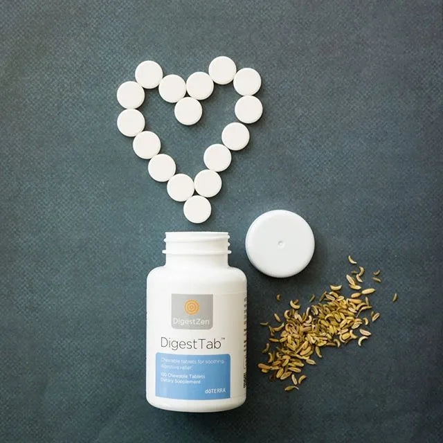 Frasco de dōTERRA DigestTab con tabletas masticables dispuestas en forma de corazón junto a semillas de hinojo sobre fondo oscuro.