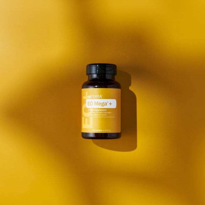 Suplemento nutricional dōTERRA EO Mega+ en frasco ámbar sobre un fondo amarillo vibrante y cálido.