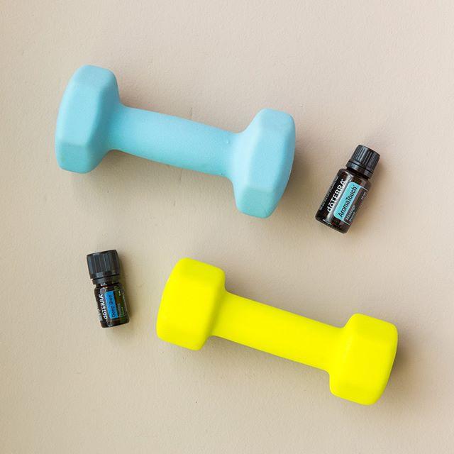 Botellas de Doterra junto a mancuernas de gimnasio, de color azul y amarillo sobre un fondo crema neutro.