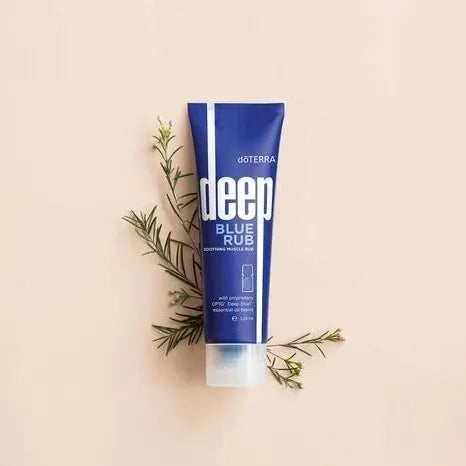 Crema calmante dōTERRA Deep Blue Rub para músculos y articulaciones junto a ramas de gaulteria sobre un fondo neutro.