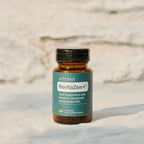 Frasco de dōTERRA RevitaZen Plus con 30 cápsulas de câmara doble sobre una superficie clara y fondo de pared de piedra.