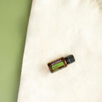 Frasco del Aceite Esencial de Albahaca dōTERRA 15ml sobre bolsa de tote de lino crema, fondo verde, vista cenital
