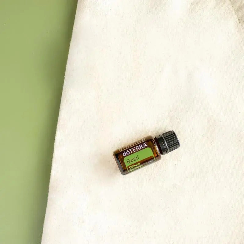Frasco del Aceite Esencial de Albahaca dōTERRA 15ml sobre bolsa de tote de lino crema, fondo verde, vista cenital