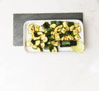 Vista aérea del Aceite Esencial de Albahaca dōTERRA 15ml sobre plato blanco con calabacín a la plancha y rodaja de lima, base de pizarra gris