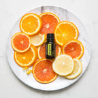 Vista aérea del Aceite Esencial de Bergamota dōTERRA 15ml sobre plato de mármol blanco rodeado de rodajas de naranja, pomelo y limón