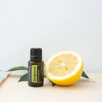Frasco del Aceite Esencial de Bergamota dōTERRA 15ml sobre tabla de madera con mitad de fruta de bergamota y hojas verdes, fondo gris claro
