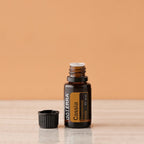 Frasco abierto del Aceite Esencial de Casia dōTERRA 15ml con tapa a un lado sobre superficie de mármol, fondo melocotón