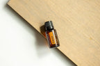 Frasco del Aceite Esencial de Casia dōTERRA 15ml sobre tabla de madera natural en ángulo, superficie blanca