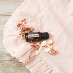 Frasco del Aceite Esencial de Cedro dōTERRA 15ml sobre tela de lino rosa arrugada con virutas de cedro esparcidas, superficie de madera