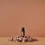 Frasco del Aceite Esencial de Cedro dōTERRA 15ml rodeado de virutas de madera de cedro sobre superficie beige, fondo terracota