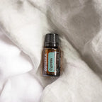 Frasco del Aceite Esencial de Ciprés dōTERRA 15ml sobre tela de gasa blanca arrugada, etiqueta teal visible