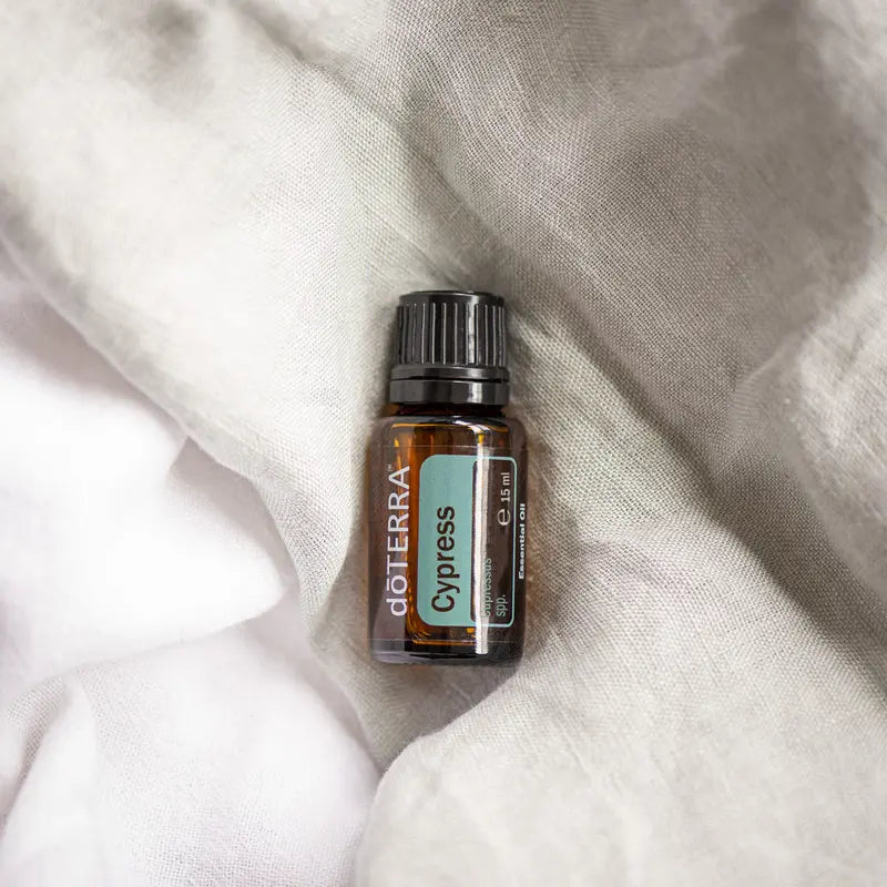Frasco del Aceite Esencial de Ciprés dōTERRA 15ml sobre tela de gasa blanca arrugada, etiqueta teal visible