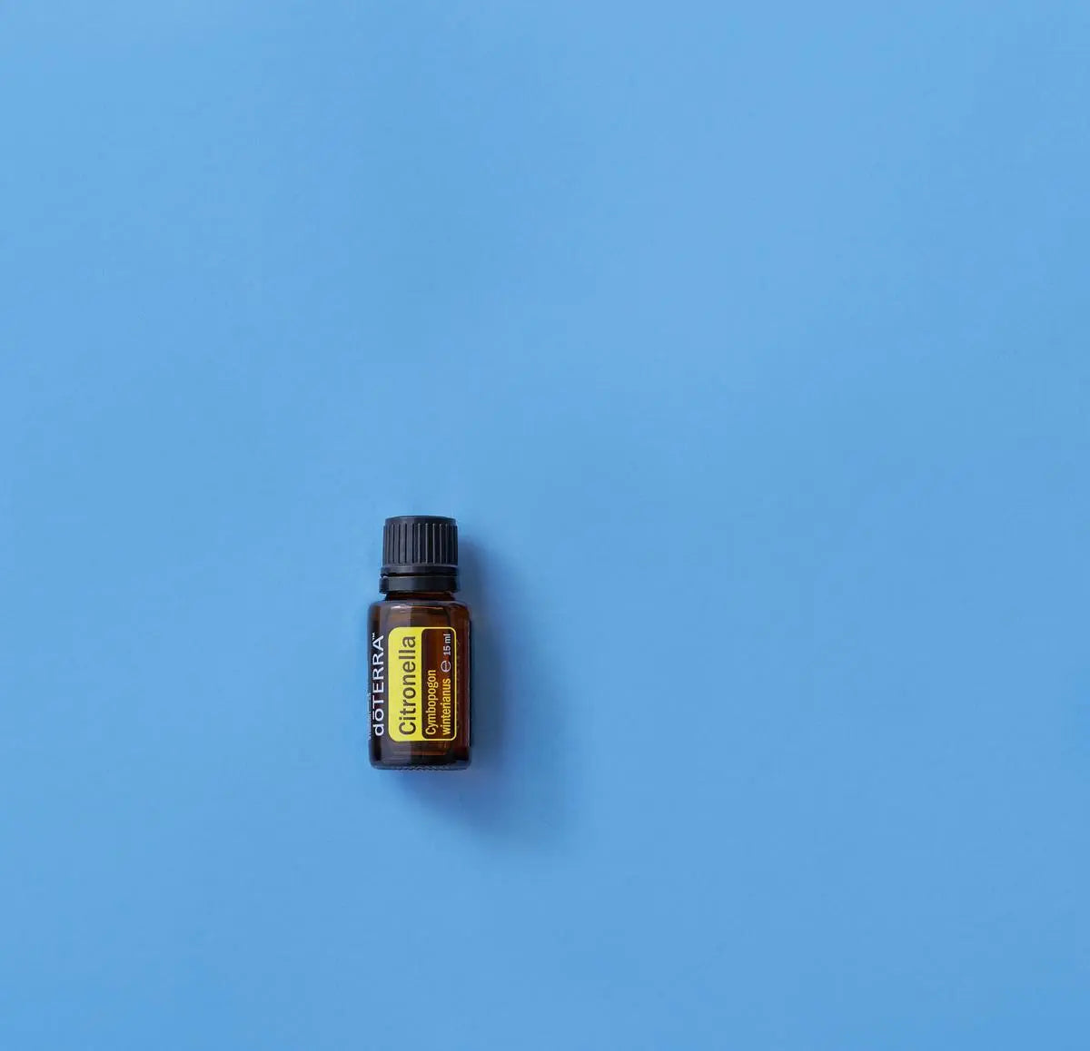 Frasco del Aceite Esencial de Citronela dōTERRA 15ml centrado sobre fondo liso azul cielo, composición minimalista
