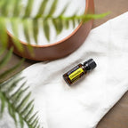 Frasco del Aceite Esencial de Citronela dōTERRA 15ml sobre tela de lino blanca con sombra de helecho proyectada, cuenco de terracota al fondo