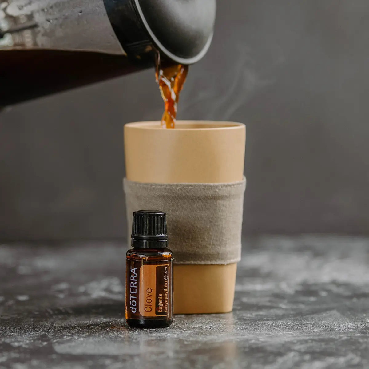 Aceite esencial de clavo dōTERRA 15 ml junto a una taza de café recién servido sobre superficie de piedra gris