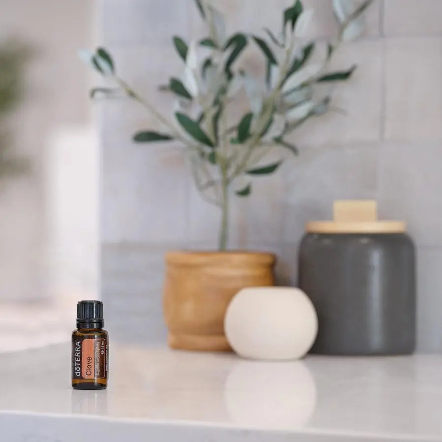 Aceite esencial de clavo dōTERRA 15 ml en encimera junto a difusor aromático blanco y plantas decorativas
