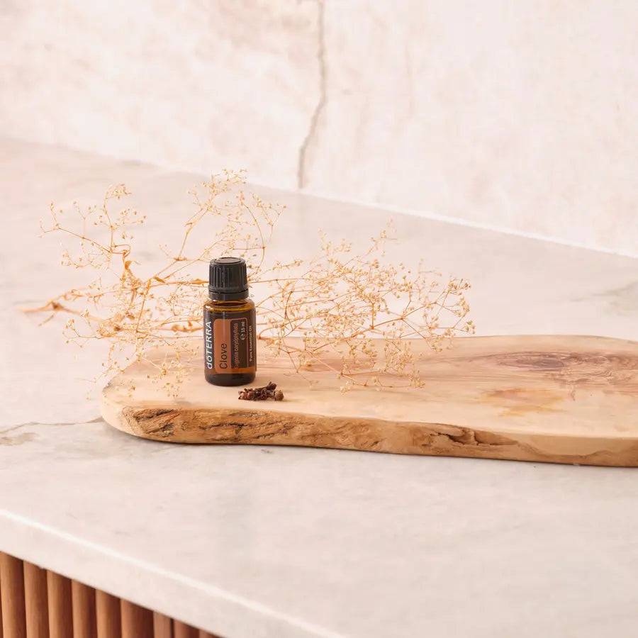 Aceite esencial de clavo dōTERRA 15 ml sobre tabla de madera rústica con flores secas y clavos de especia