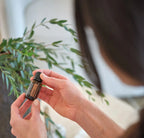 Manos sosteniendo el aceite esencial de clavo dōTERRA 15 ml con fondo de vegetación verde