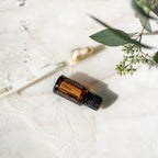 Frasco de aceite esencial de clavo dōTERRA 15 ml sobre mármol blanco con gotas de agua y hojas de eucalipto