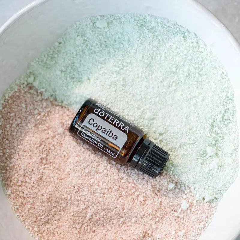 Vista cenital del Aceite Esencial de Copaiba dōTERRA 15ml en cuenco blanco con sales de baño bicolor: rosa himalaya y verde/blanca