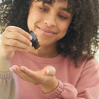 Mujer con cabello rizado y jersey rosa aplicando gota de Espicanardo dōTERRA 5ml en la palma