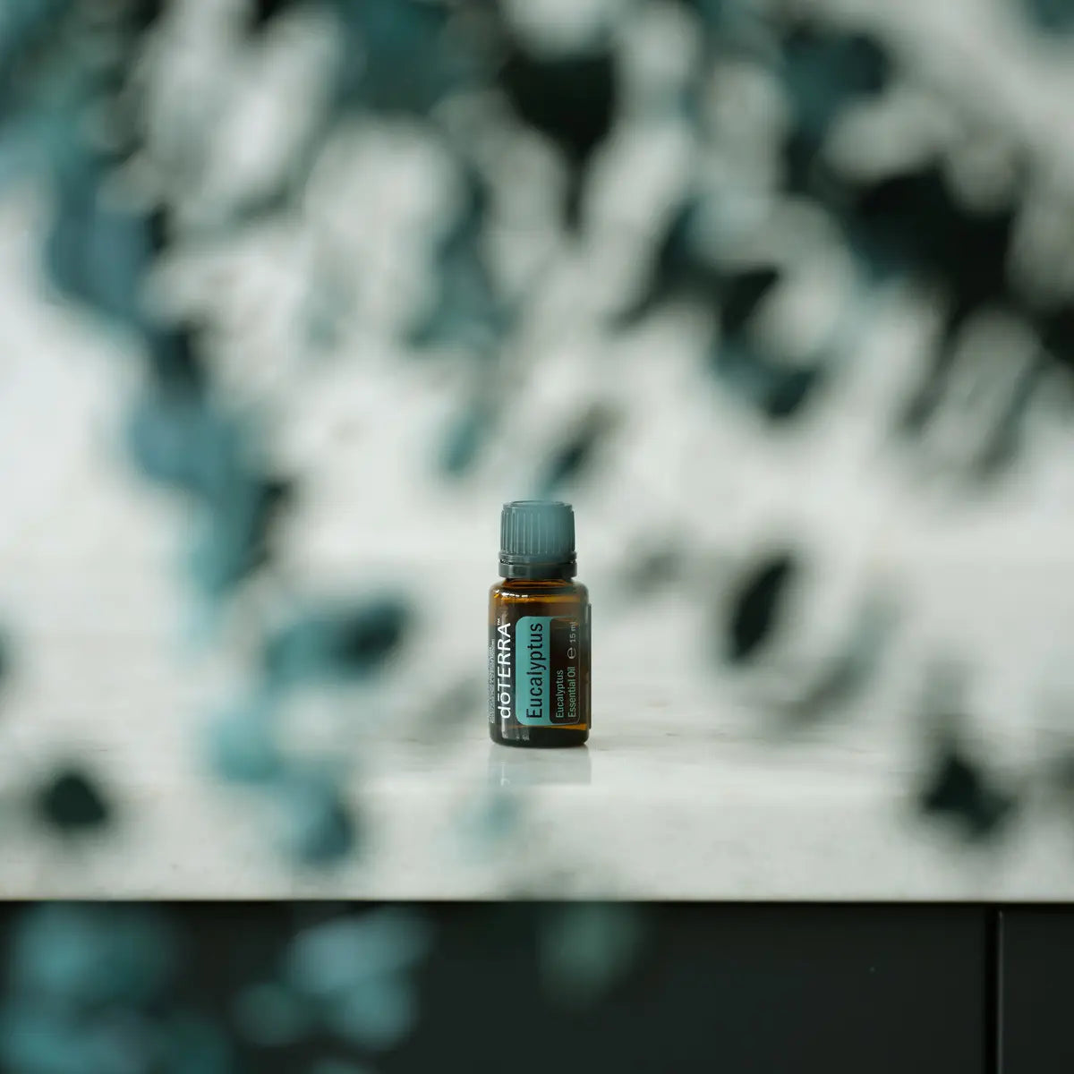 Frasco de aceite esencial de Eucalipto doTERRA 15ml centrado en superficie gris con fondo de hojas de eucalipto desenfocadas en tonos azul grisaceo