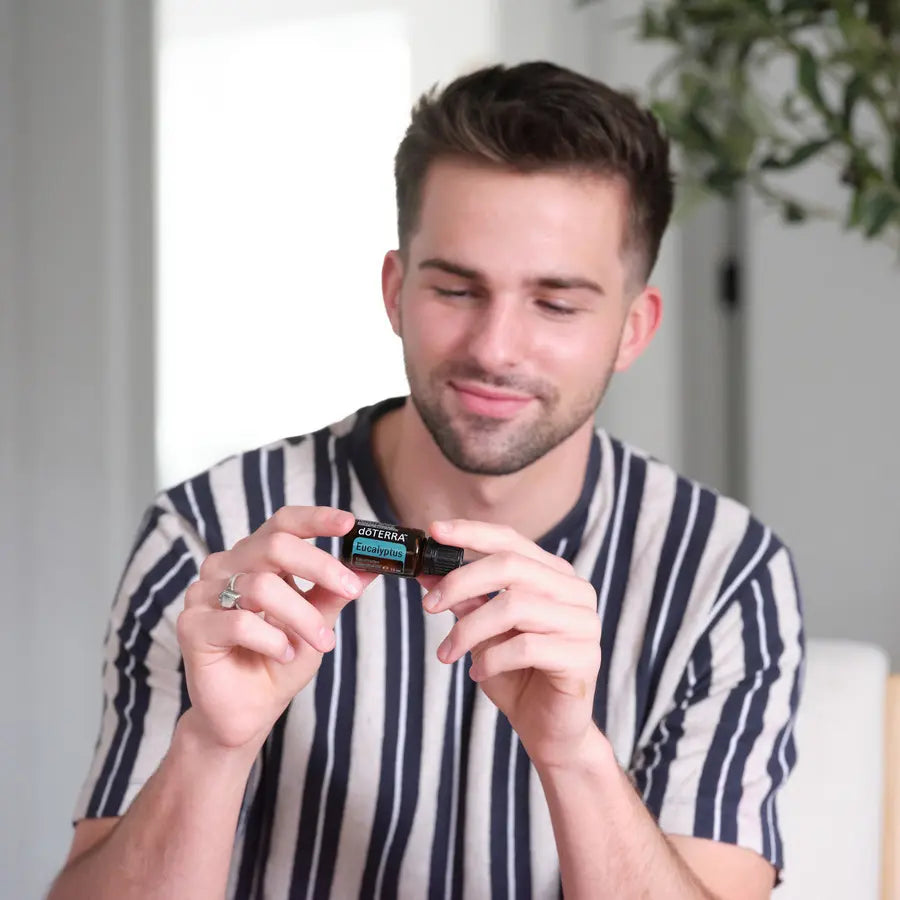 Hombre con camiseta a rayas azul marino sosteniendo y oliendo el aceite esencial de Eucalipto doTERRA 15ml en interior luminoso