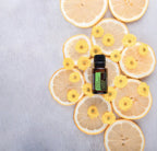 Aceite esencial de eucalipto limón dōTERRA 15ml sobre madera blanca rodeado de rodajas secas de limón y pequeñas flores amarillas silvestres, flat lay cenital