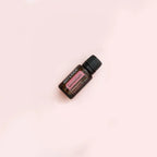 Frasco de aceite esencial de geranio dōTERRA 15ml en posición diagonal sobre fondo liso rosa pálido, composición minimalista de estudio