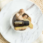 Aceite esencial de jengibre dōTERRA 15ml en cuenco de mármol blanco con rodajas y raíz de jengibre fresco sobre base de ratán tejido