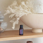 Frasco de aceite esencial de Lavanda doTERRA 15ml en estante de madera junto a cuenco beige y flores blancas secas silvestres