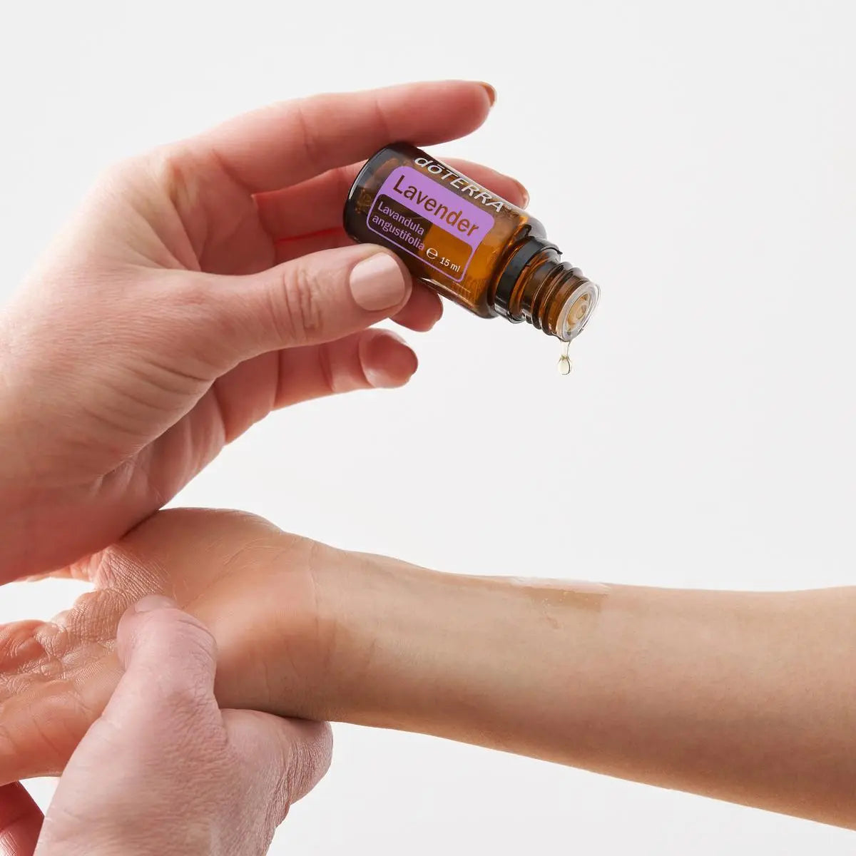 Aceite esencial de Lavanda doTERRA 15ml inclinado sobre la muneca con una gota cayendo, fondo blanco neutro