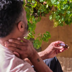 Hombre sentado al aire libre bajo arbol aplicando aceite esencial de Lavanda doTERRA 15ml en el cuello con hojas verdes al fondo