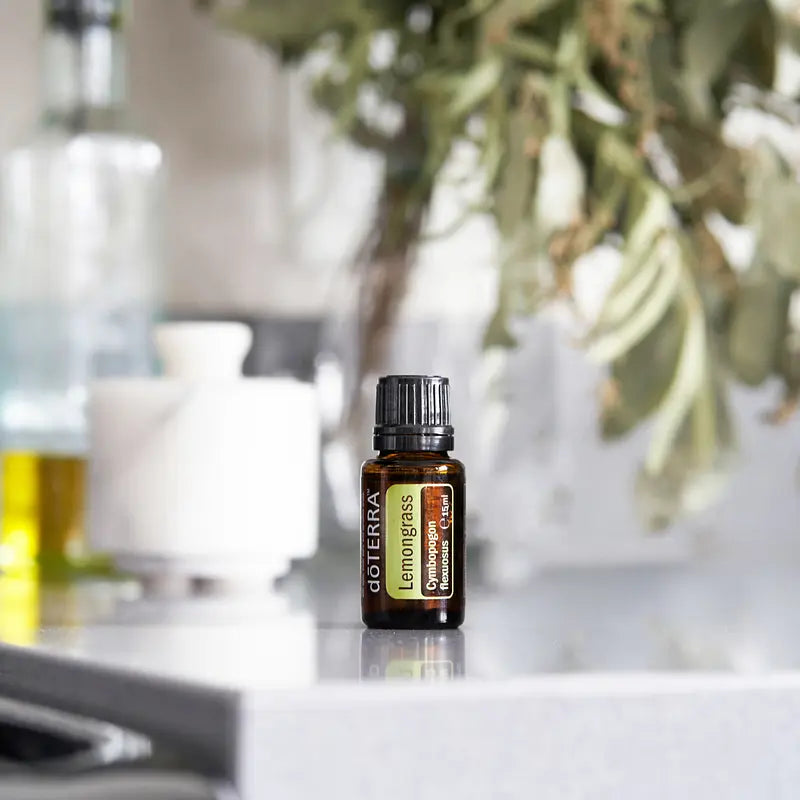 Aceite esencial de Lemongrass doTERRA 15ml sobre encimera de marmol blanco junto a difusor ultrasonico y ramas de olivo al fondo