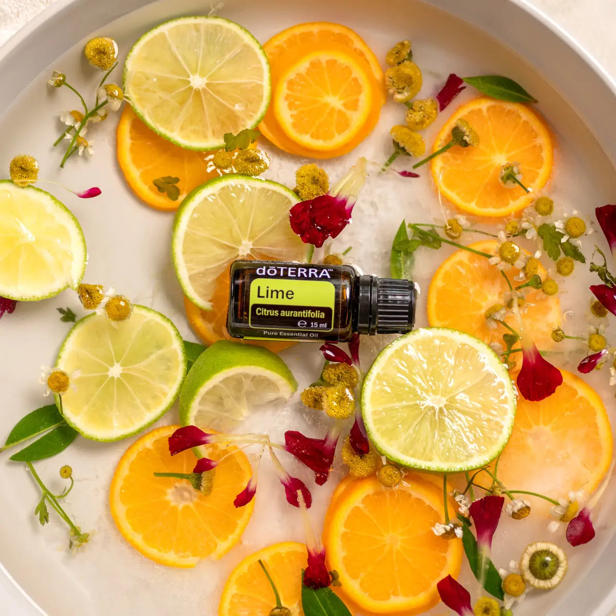 Aceite Esencial Lima dōTERRA 15ml en cuenco con rodajas de lima y naranja con flores cenital