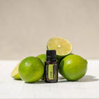 Aceite Esencial Lima dōTERRA 15ml junto a limas frescas enteras y cortadas sobre fondo beige