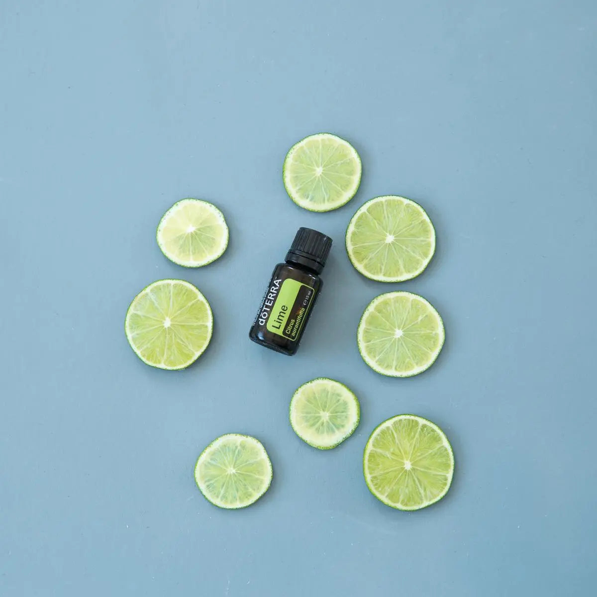 Aceite Esencial Lima dōTERRA 15ml con rodajas de lima sobre fondo azul grisáceo cenital