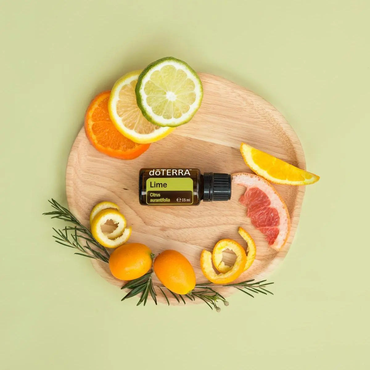 Aceite Esencial Lima dōTERRA 15ml en tabla de madera con cítricos variados y romero sobre fondo verde