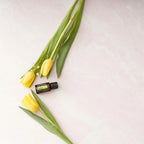 Aceite Esencial Lima dōTERRA 15ml con tulipanes amarillos sobre fondo rosa claro