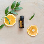 Aceite Esencial Mandarina dōTERRA 15ml en disco de madera con rodajas de naranja y ramas verdes cenital