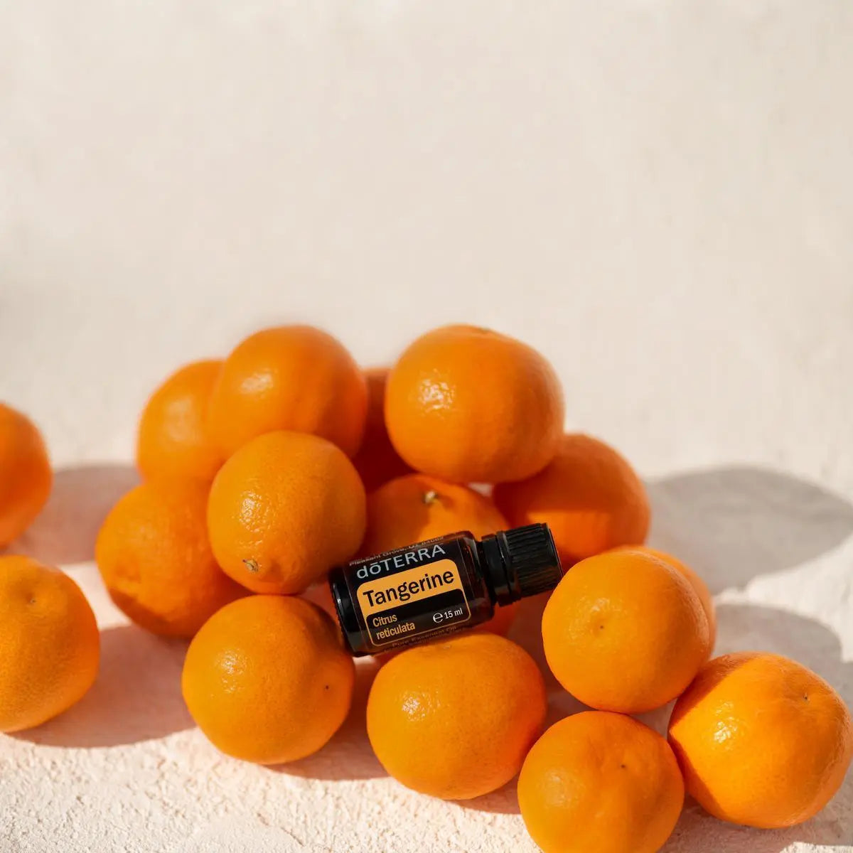 Aceite Esencial Mandarina dōTERRA 15ml sobre montón de mandarinas enteras en superficie arena
