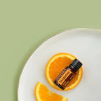 Aceite Esencial Mandarina Tangerine dōTERRA 15ml en plato blanco con rodaja de mandarina sobre fondo verde salvia