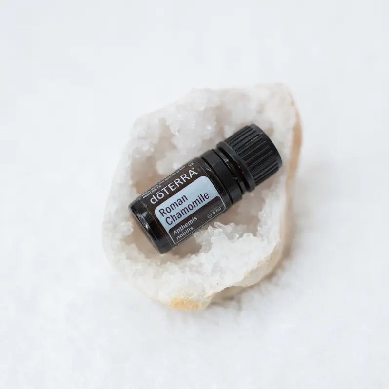 Aceite esencial de Manzanilla Romana dōTERRA 5ml apoyado en geoda de cuarzo blanco sobre fondo blanco
