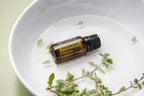 Aceite esencial de Mejorana dōTERRA 15ml en cuenco blanco con ramita de mejorana fresca