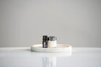 Aceite esencial de Melissa dōTERRA 5ml junto a tarro de crema sobre bandeja circular de mármol blanco, fondo gris