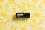 Aceite esencial de Melissa dōTERRA 5ml sobre tela estampada floral en tonos amarillos y blancos, flat lay