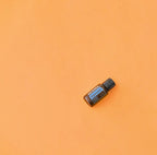 Aceite esencial Peppermint dōTERRA 15ml en diagonal sobre fondo liso naranja mandarina vibrante, composición minimalista