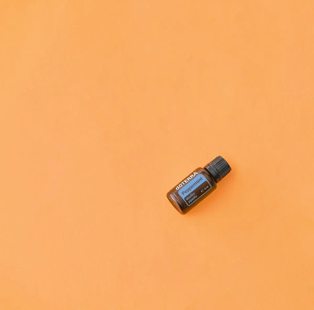 Aceite esencial Peppermint dōTERRA 15ml en diagonal sobre fondo liso naranja mandarina vibrante, composición minimalista