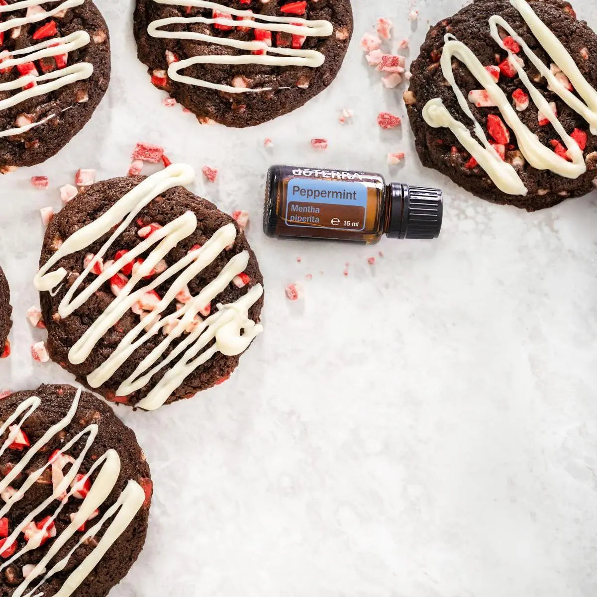 Aceite esencial Peppermint dōTERRA 15ml entre galletas de chocolate, candy cane y glaseado blanco sobre mármol