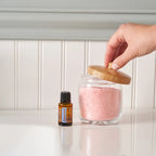 Aceite esencial Peppermint dōTERRA 15ml junto a tarro de vidrio con tapa de bambú con sales de baño rosas, encimera de cocina blanca